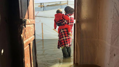 Syrian refugees wading through knee-deep water in Lebanon camps